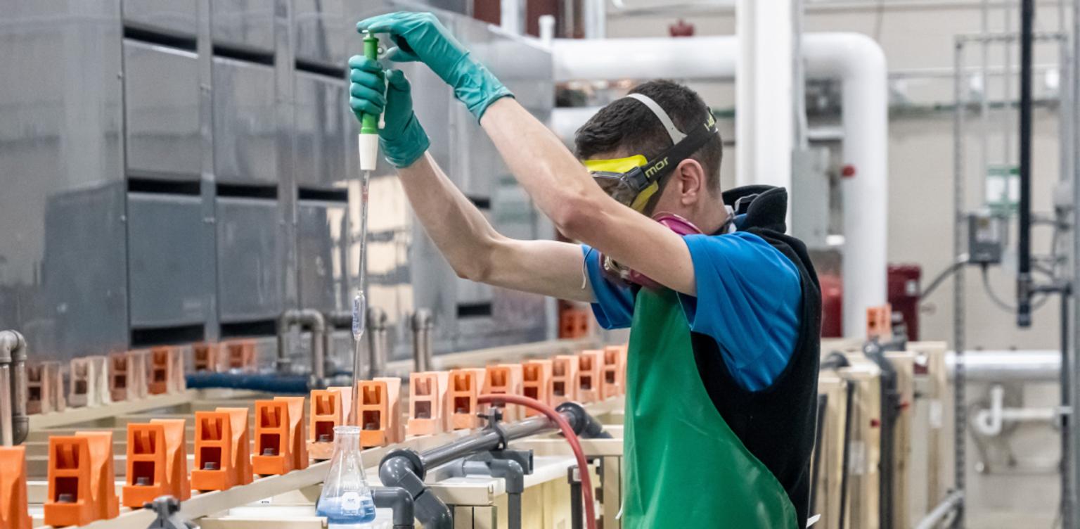 A technician takes a sample of a metal plating solution.