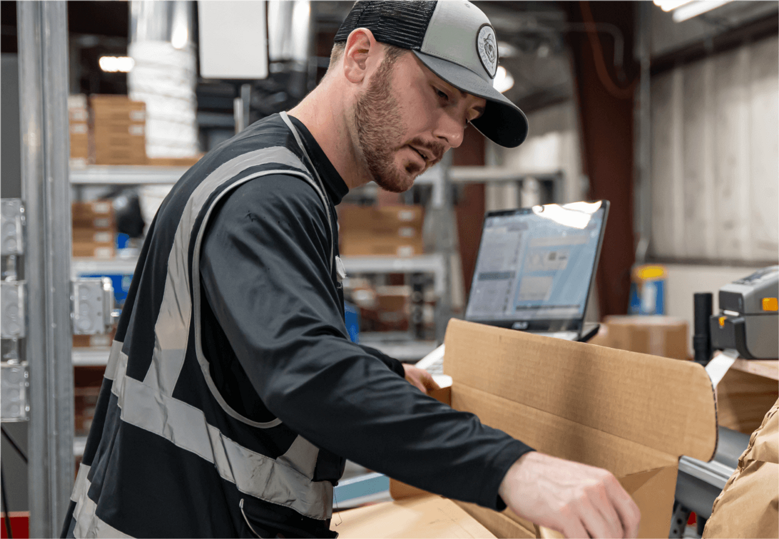 A person in a vest building a shipping box to pack a hand tool.