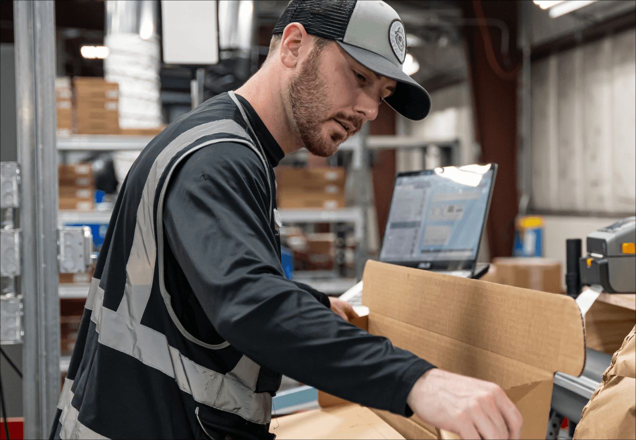 A person in a vest building a shipping box to pack a hand tool.