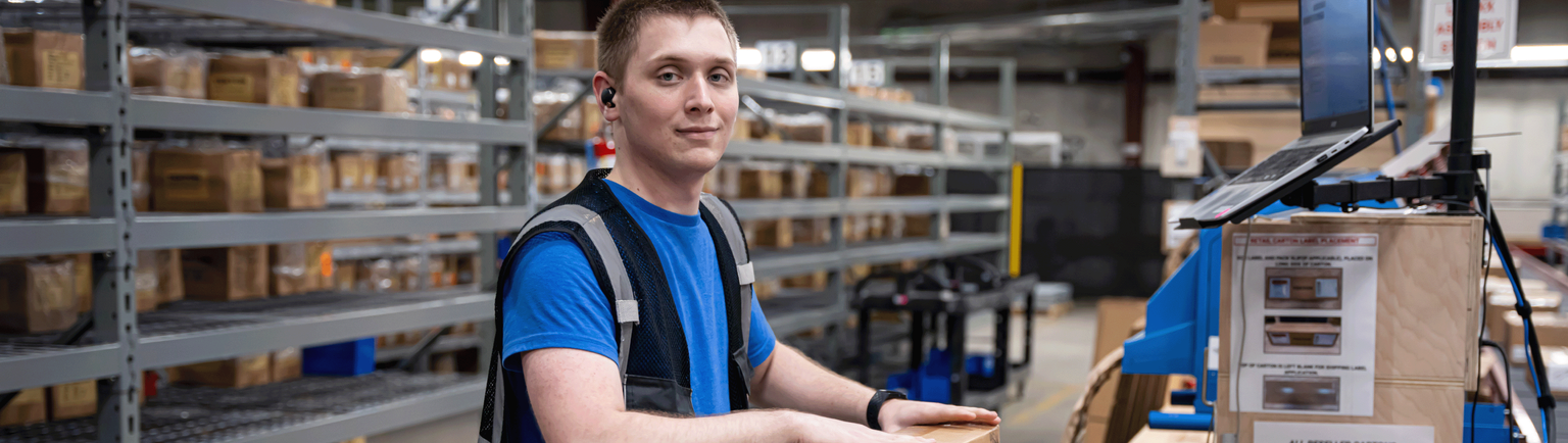 A person in a vest packing hand tools in a shipping box in the warehouse.