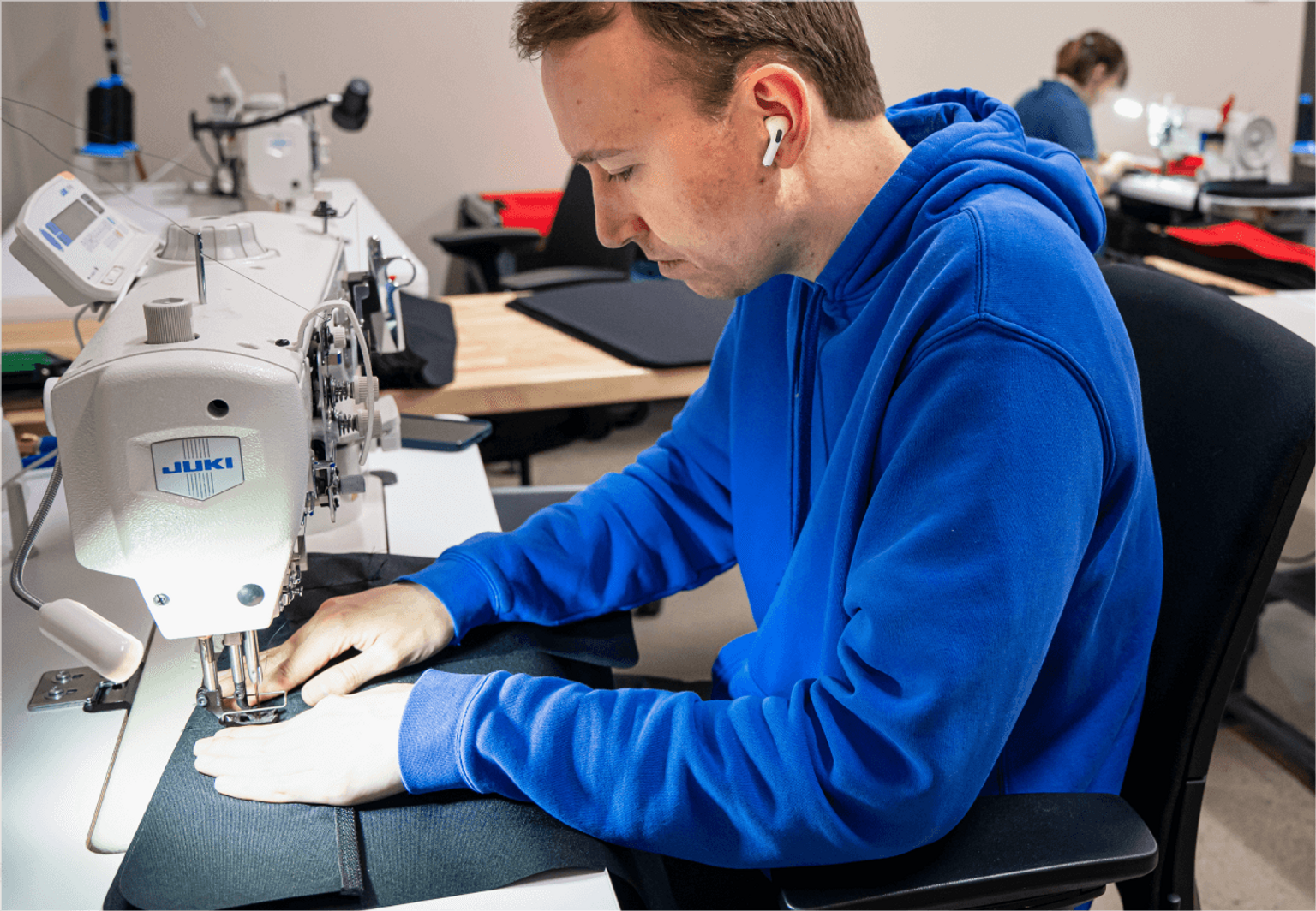 A person in a blue sweatshirt uses industrial sewing machine in sewing room.