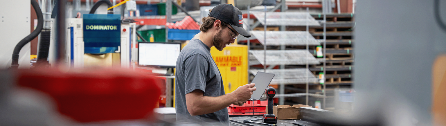 A person inspecting a hand tool in the manufacturing center surrounded by industrial machines.