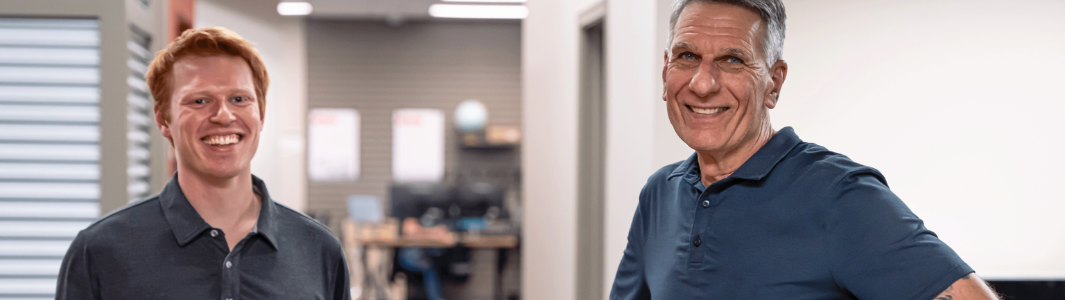 Two people in navy shirts smiling in an office.