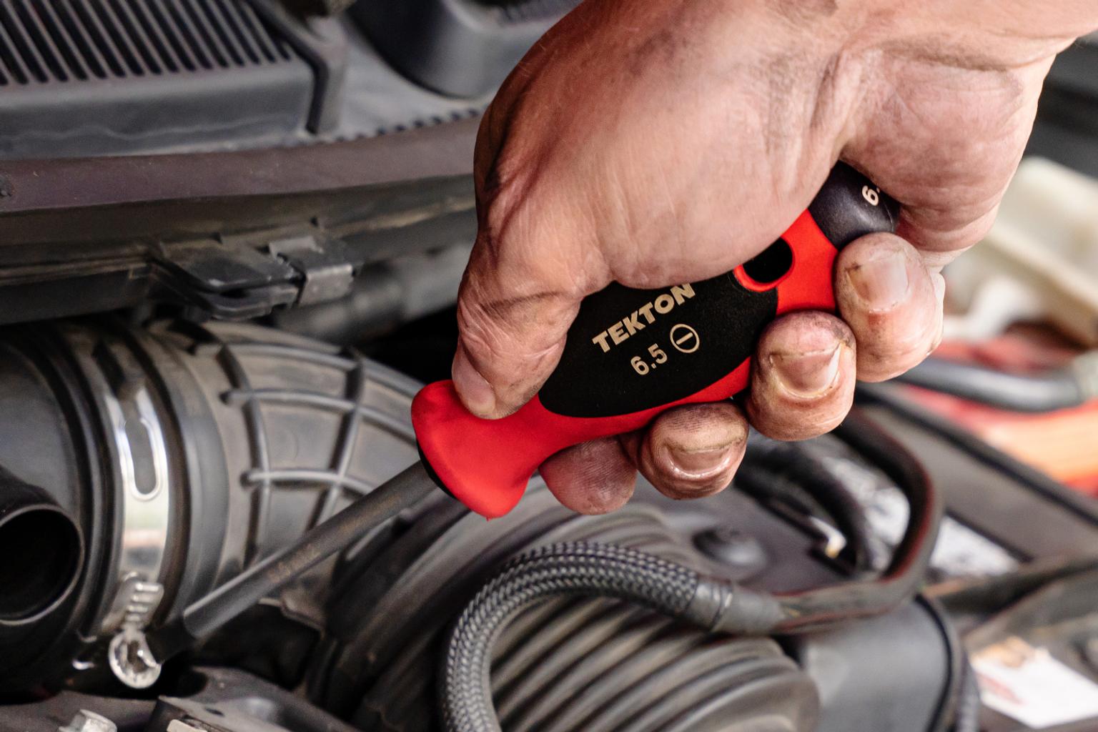 A slotted 6.5 mm screwdriver turning a screw on a vehicle.