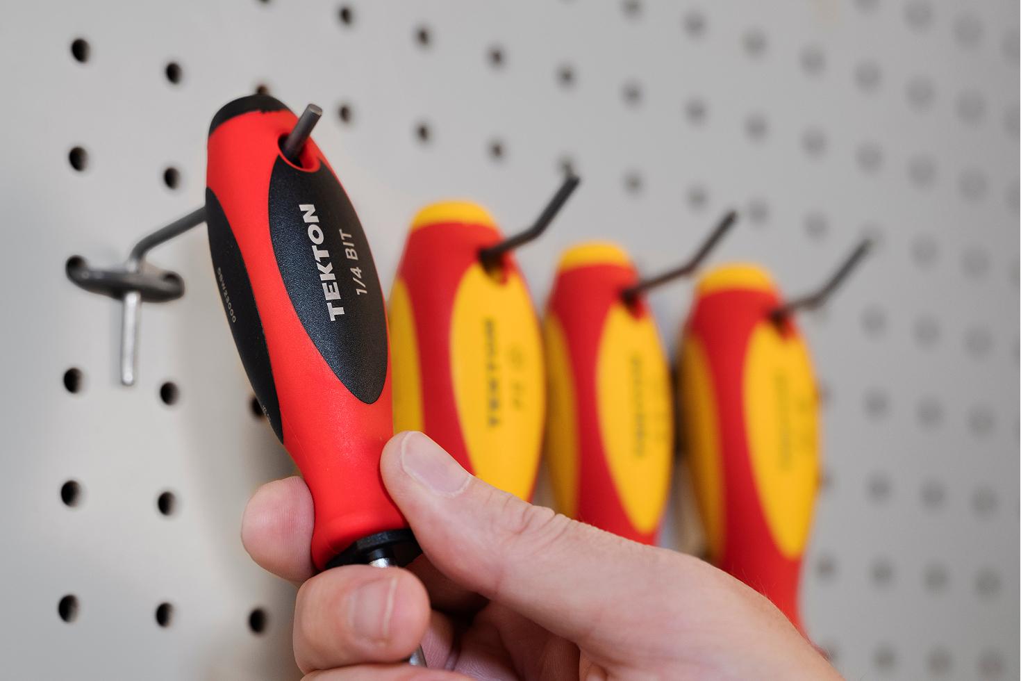 A bit driver and insulated screwdrivers hanging on a pegboard