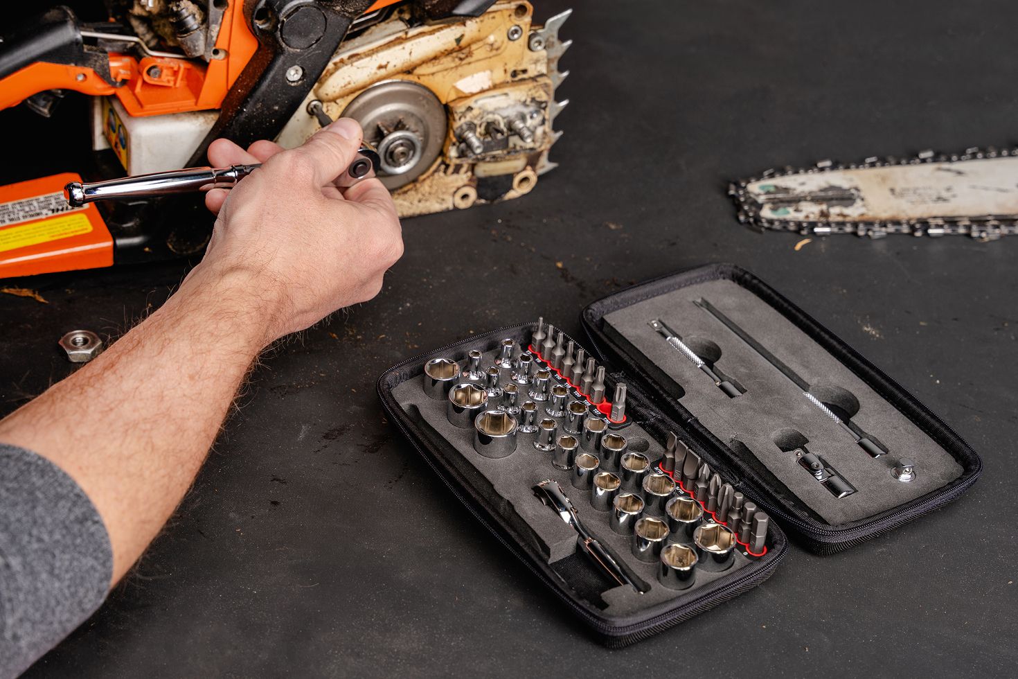 A small engine socket, bit, and ratchet set being used to repair a chainsaw.