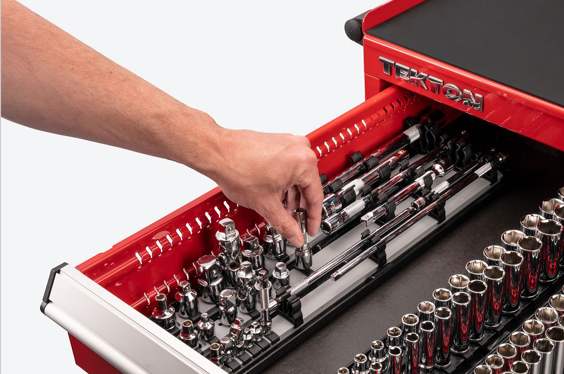 A hand lifting a hand drive extension out of an accessory set on rails. The set is in a red tool cabinet drawer.
