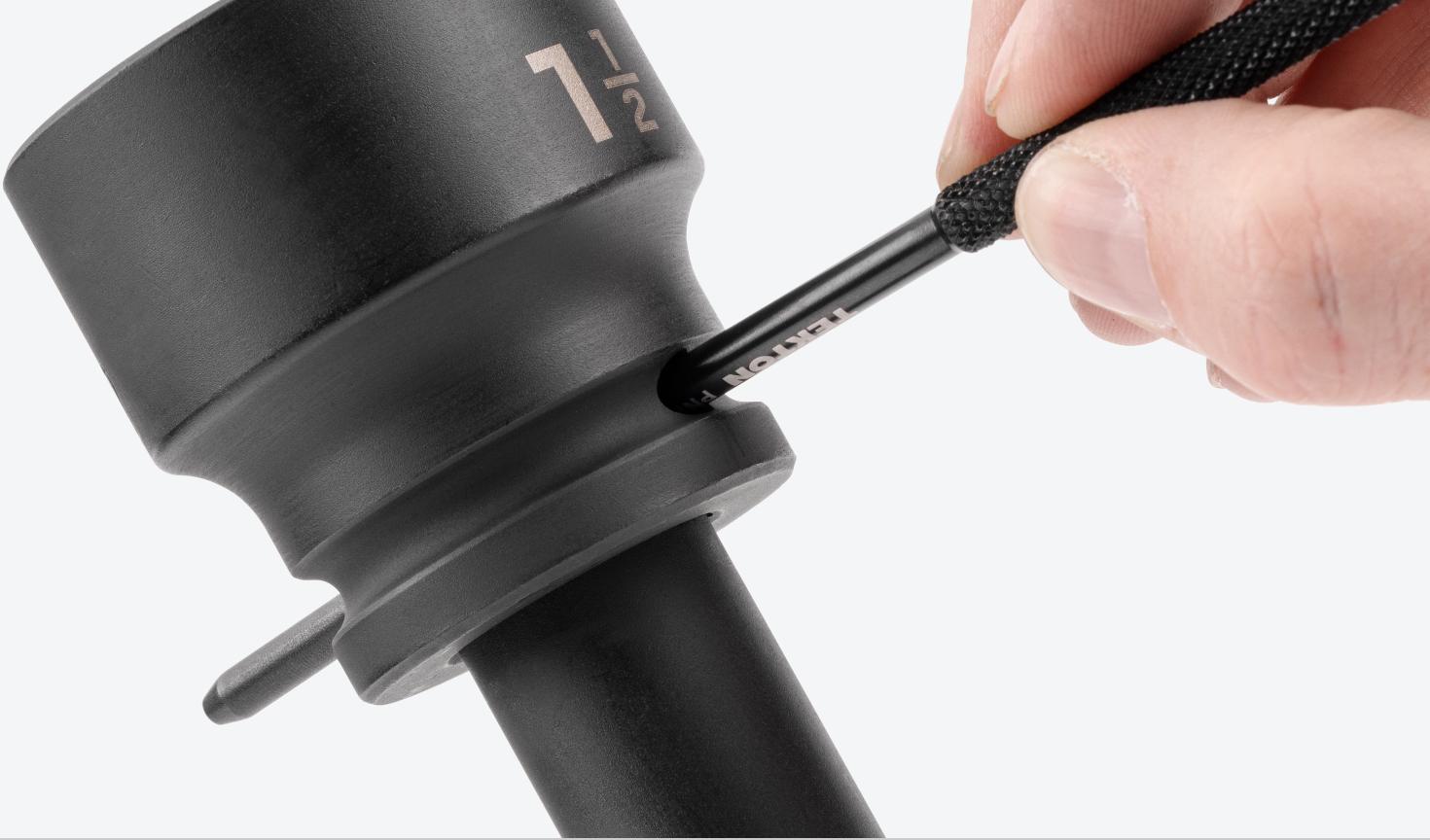 A hand holding a Socket Retaining Pin and Ring Removal Tool and pressing the retaining pin on a Tekton impact extension in order to remove an impact socket.