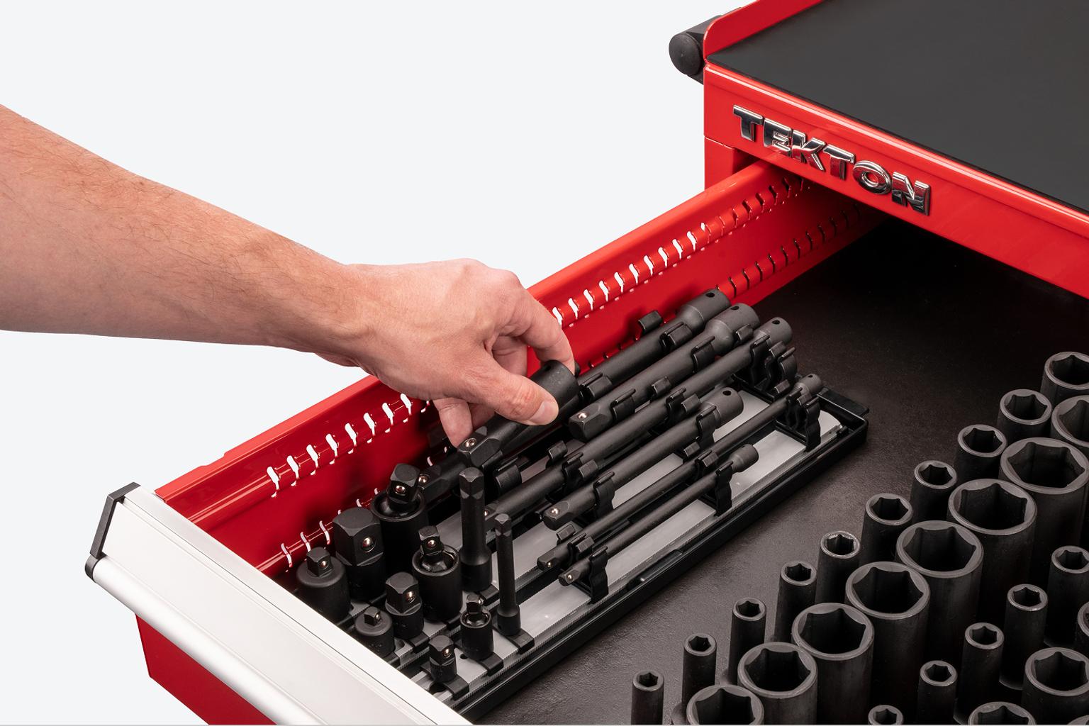 A hand lifting an impact extension out of an accessory set on rails. The set is in a red tool cabinet drawer.