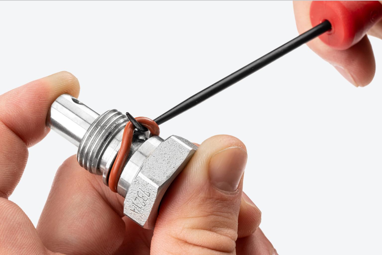 A mechanic holding a red-handled blunt point pick to remove an automotive ring.