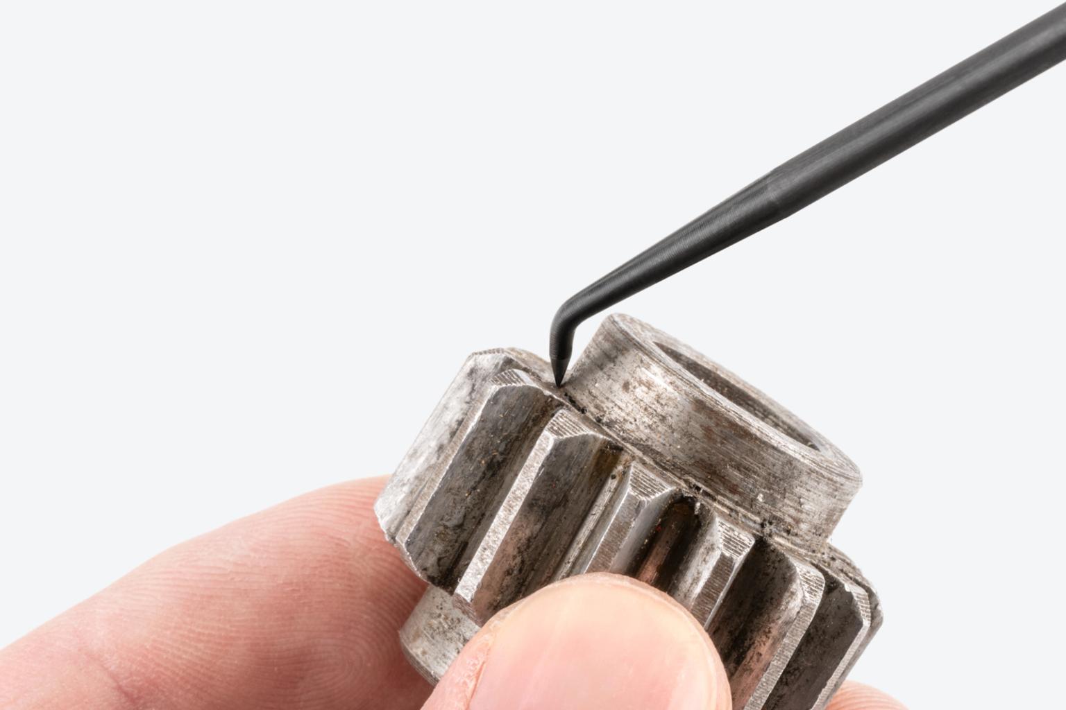 A mechanic scraping grease from a gear using a Tekton pick.