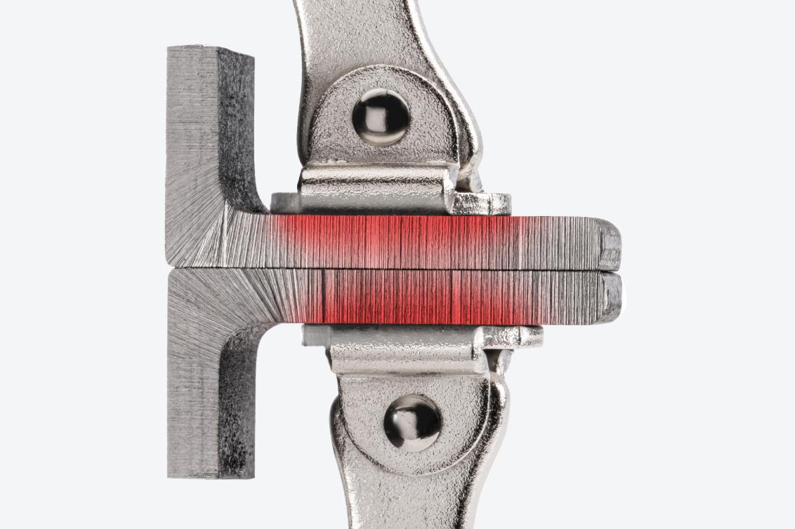 Swivel pads of a locking C-clamp clamping down on two pieces of metal. There is a red texture on the pieces of metal, showing the flat, uniform clamping force.