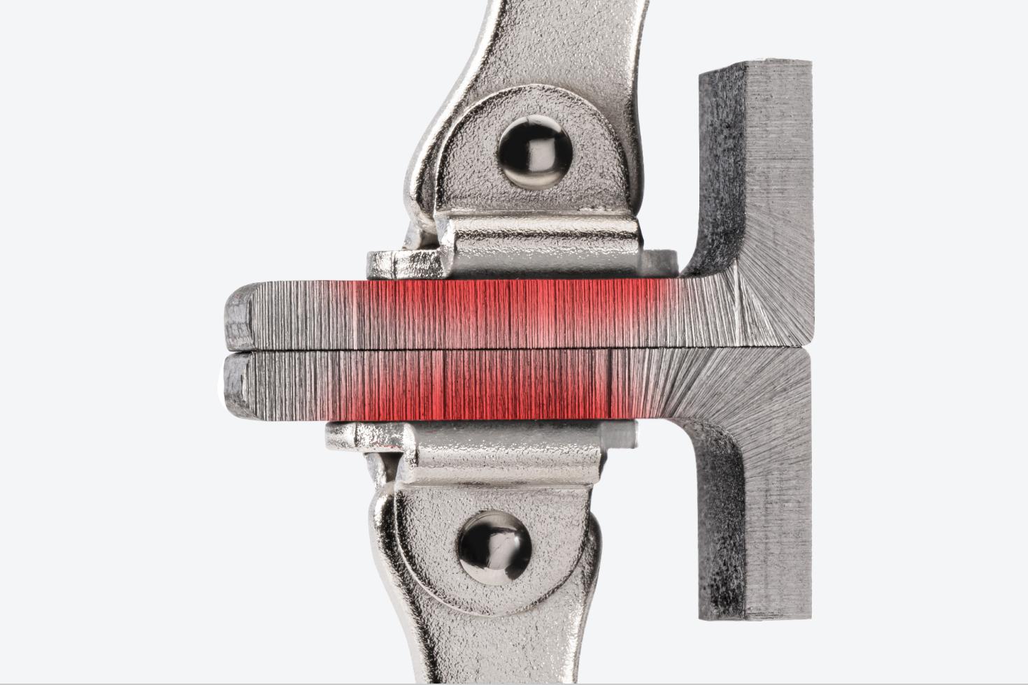 Swivel pads of a locking C-clamp clamping down on two pieces of metal. There is a red texture on the pieces of metal, showing the flat, uniform clamping force.