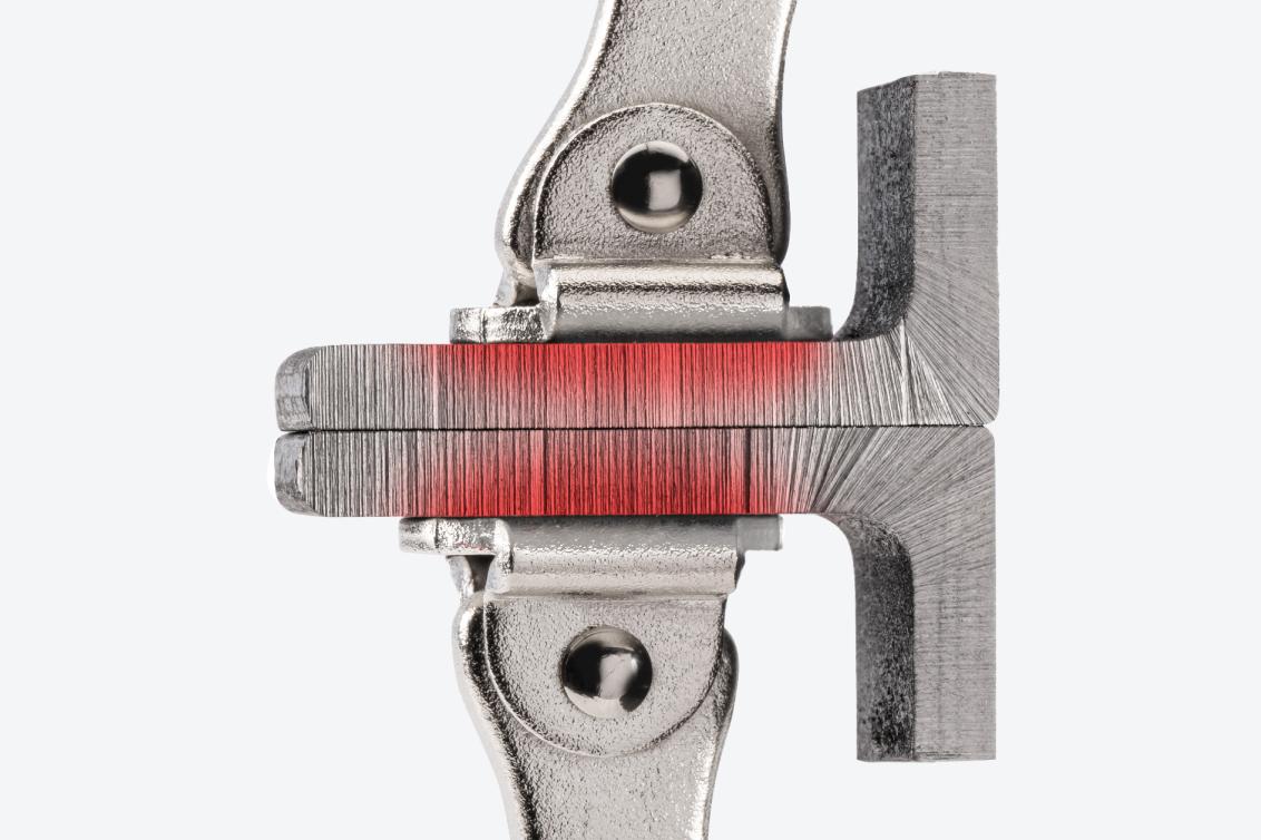 Swivel pads of a locking C-clamp clamping down on two pieces of metal. There is a red texture on the pieces of metal, showing the flat, uniform clamping force.