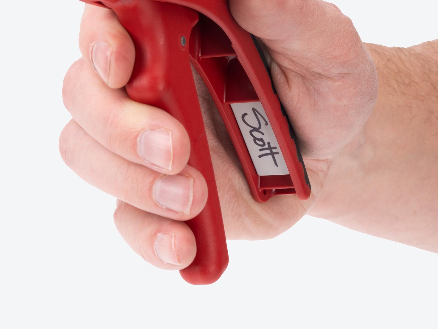 A hand holding the wire stripper, with the name "Scott" written on the panel with permanent marker