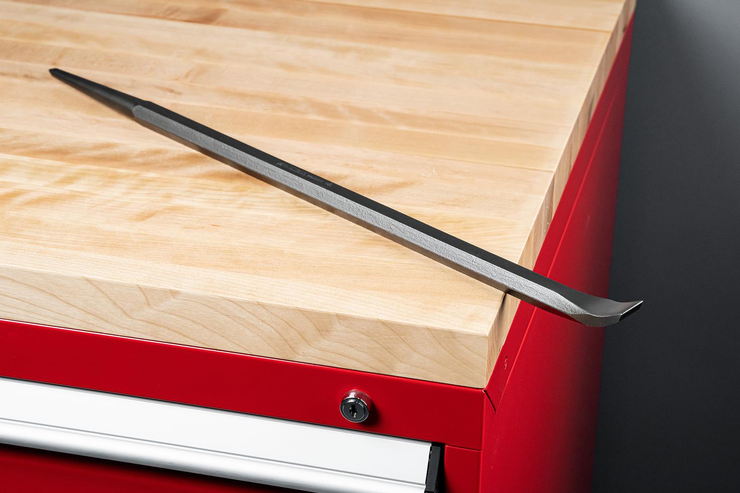 An angled end alignment pry bar sitting on top of a red tool cabinet with wood block top.