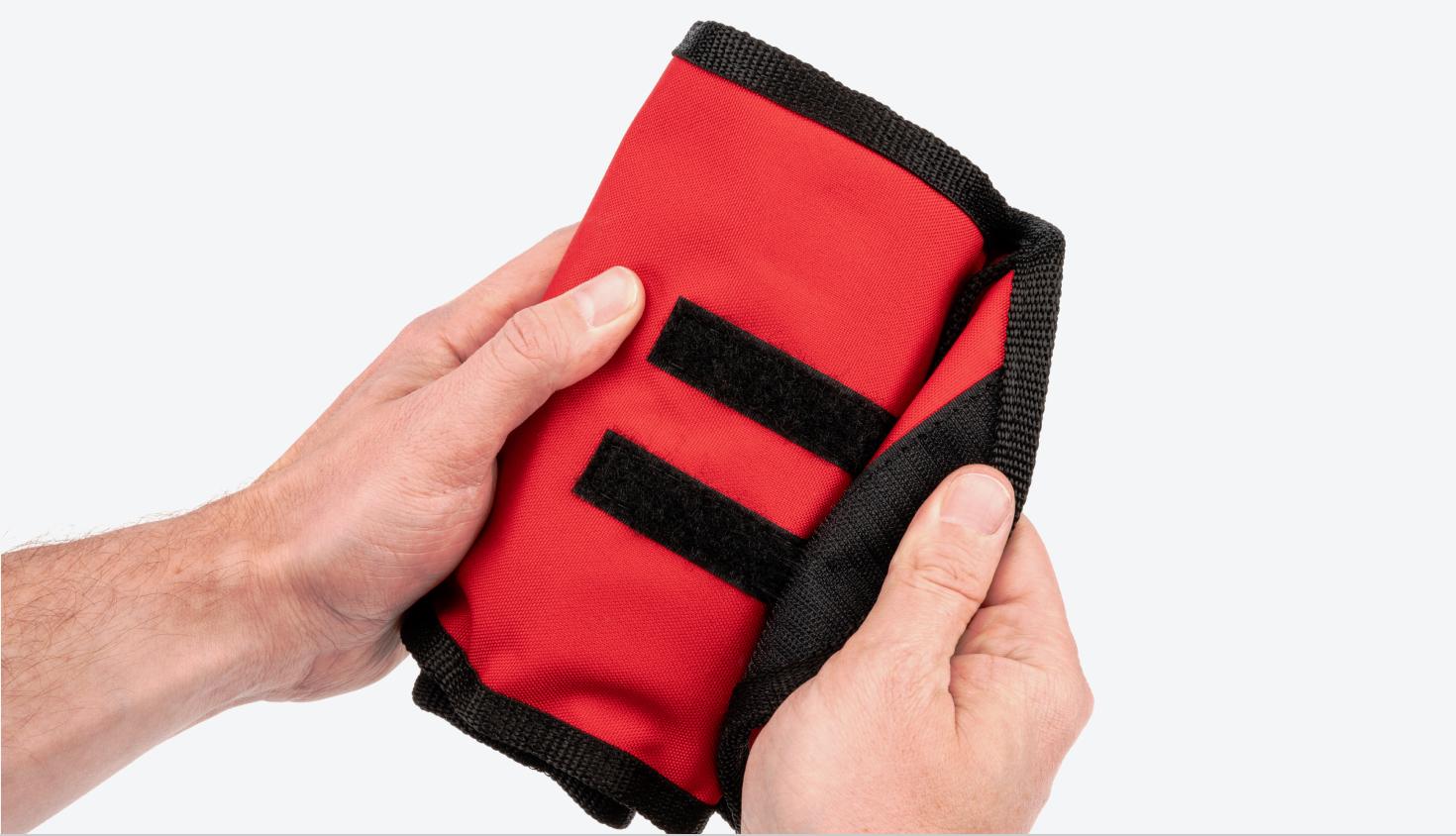 Two hands opening a red roll, showing the hook-and-loop fastener