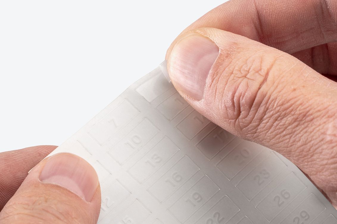 A hand pulling a label off the backer sheet.