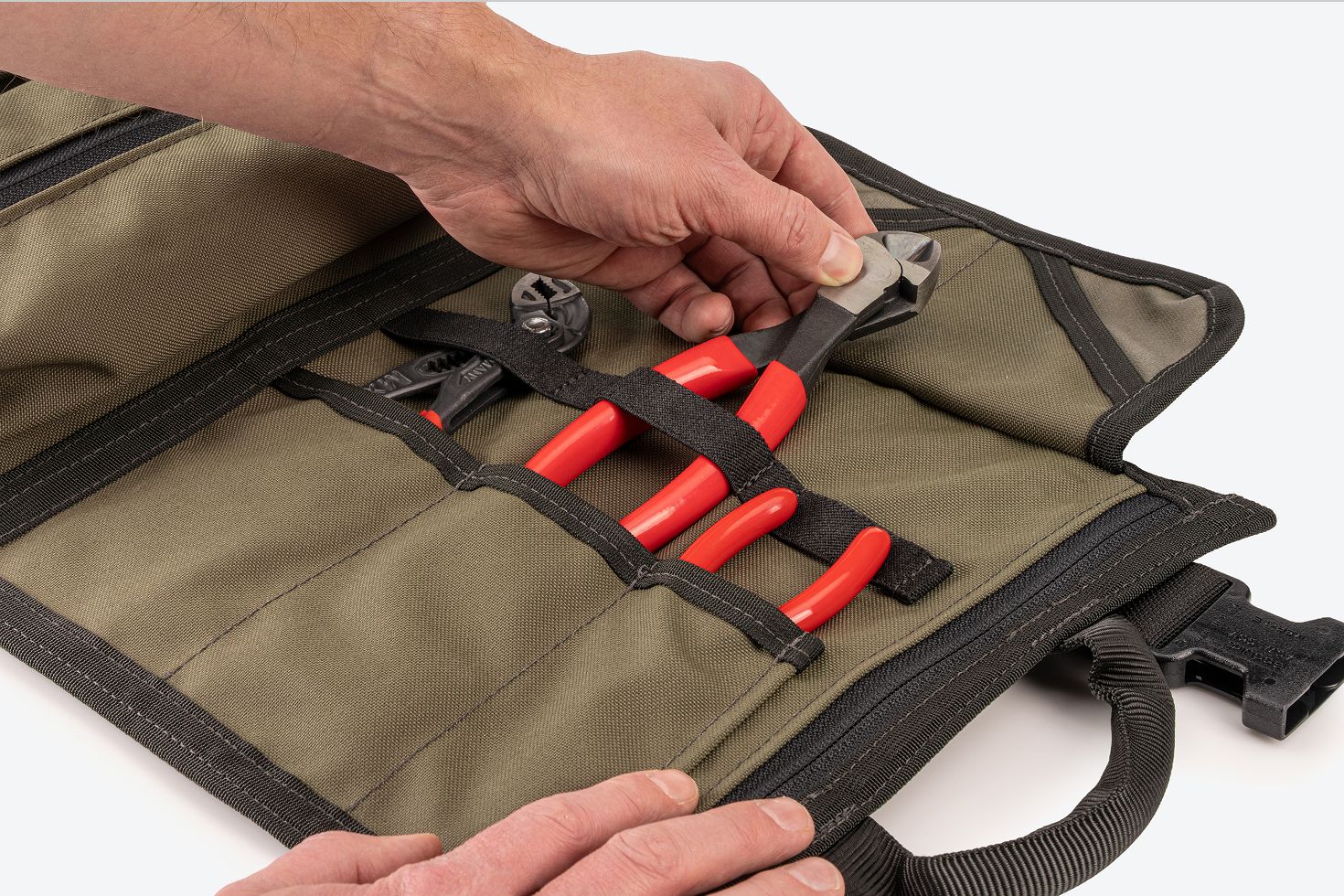 A hand pulling pliers out of an open pocket with elastic strap