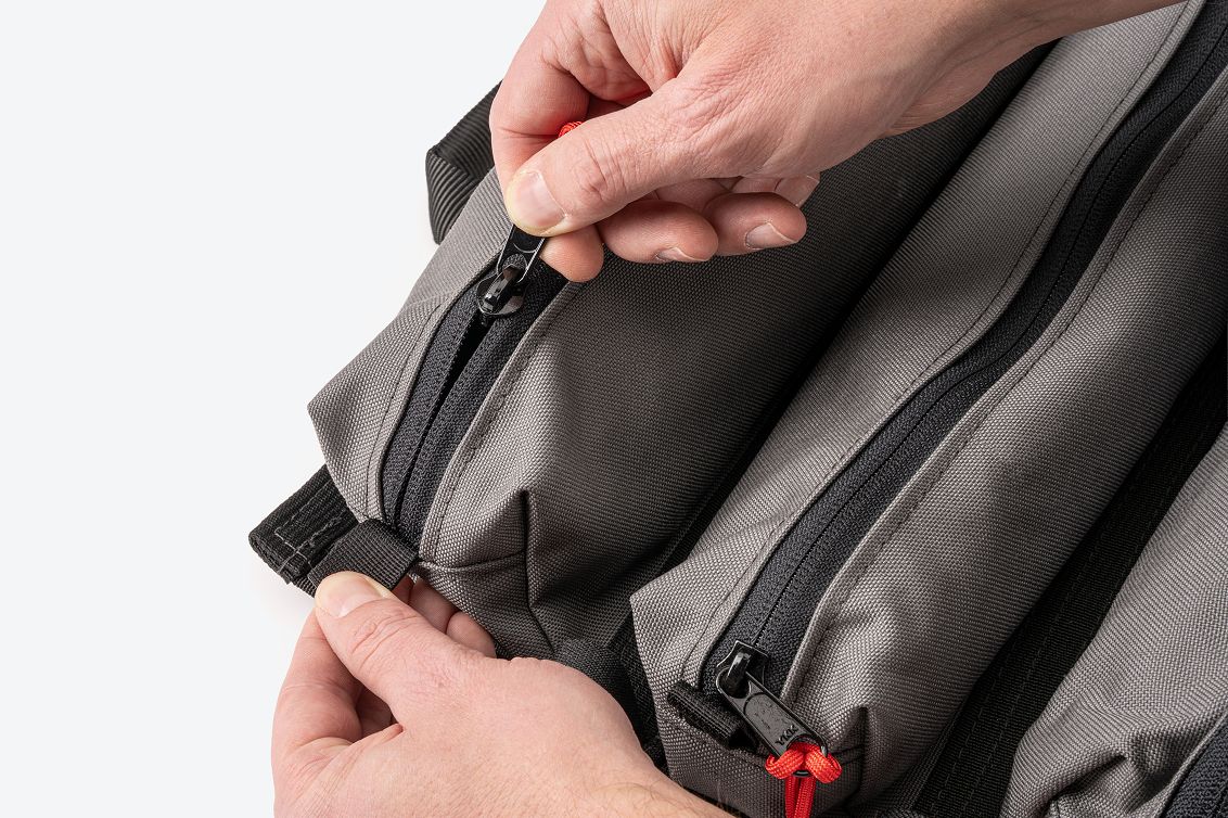 A person closing the zipper on a gray MTR pouch while holding the tab on the end of the pouch
