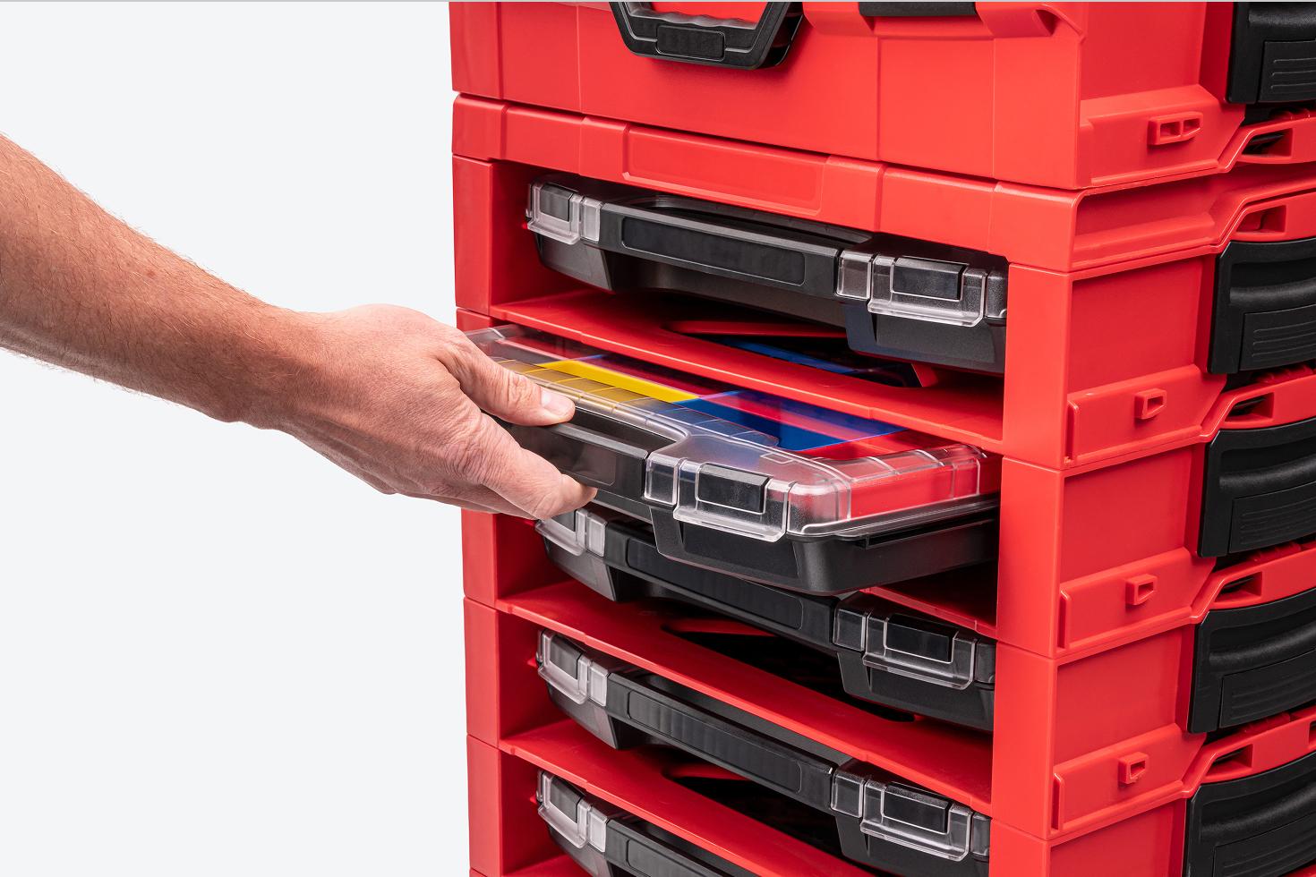 A hand pulling a shallow lidded drawer with bins out of a larger stack