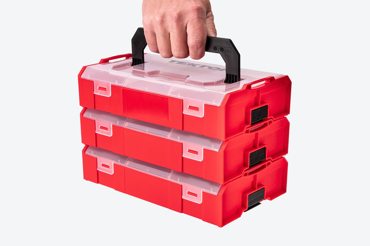 A hand carrying three red mini stacking tool boxes that are latched together.