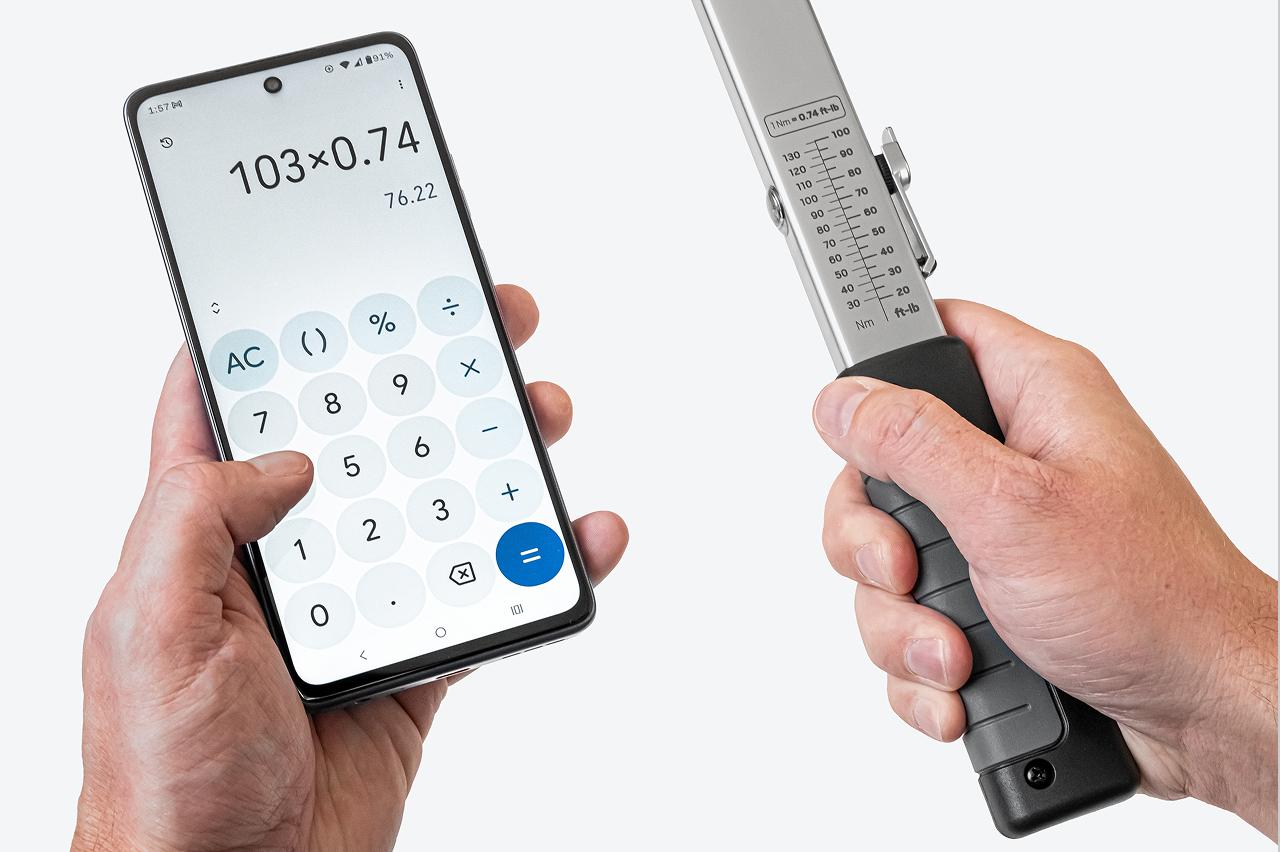 One hand holding a phone with a calculator app, the other holding a torque wrench with the scale visible