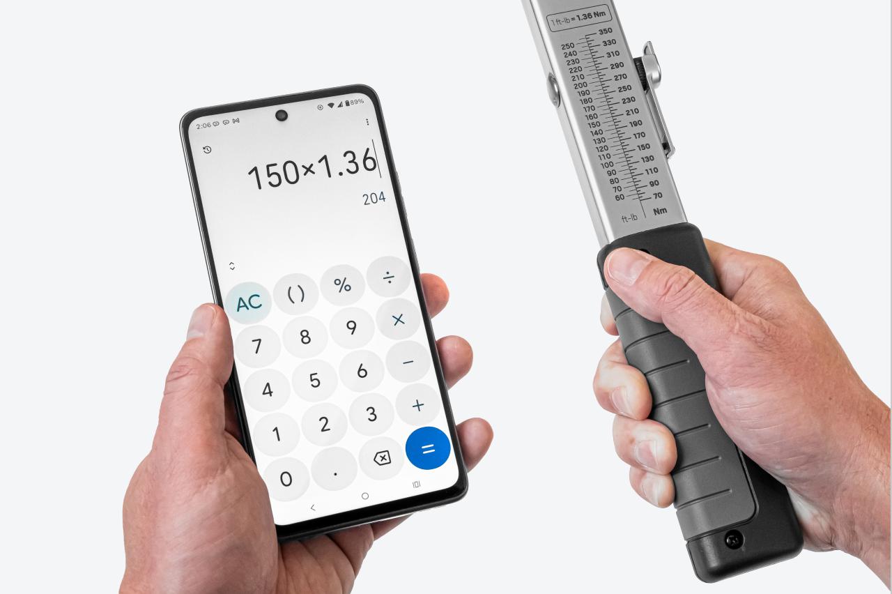 One hand holding a phone with a calculator app, the other holding a torque wrench with the scale visible