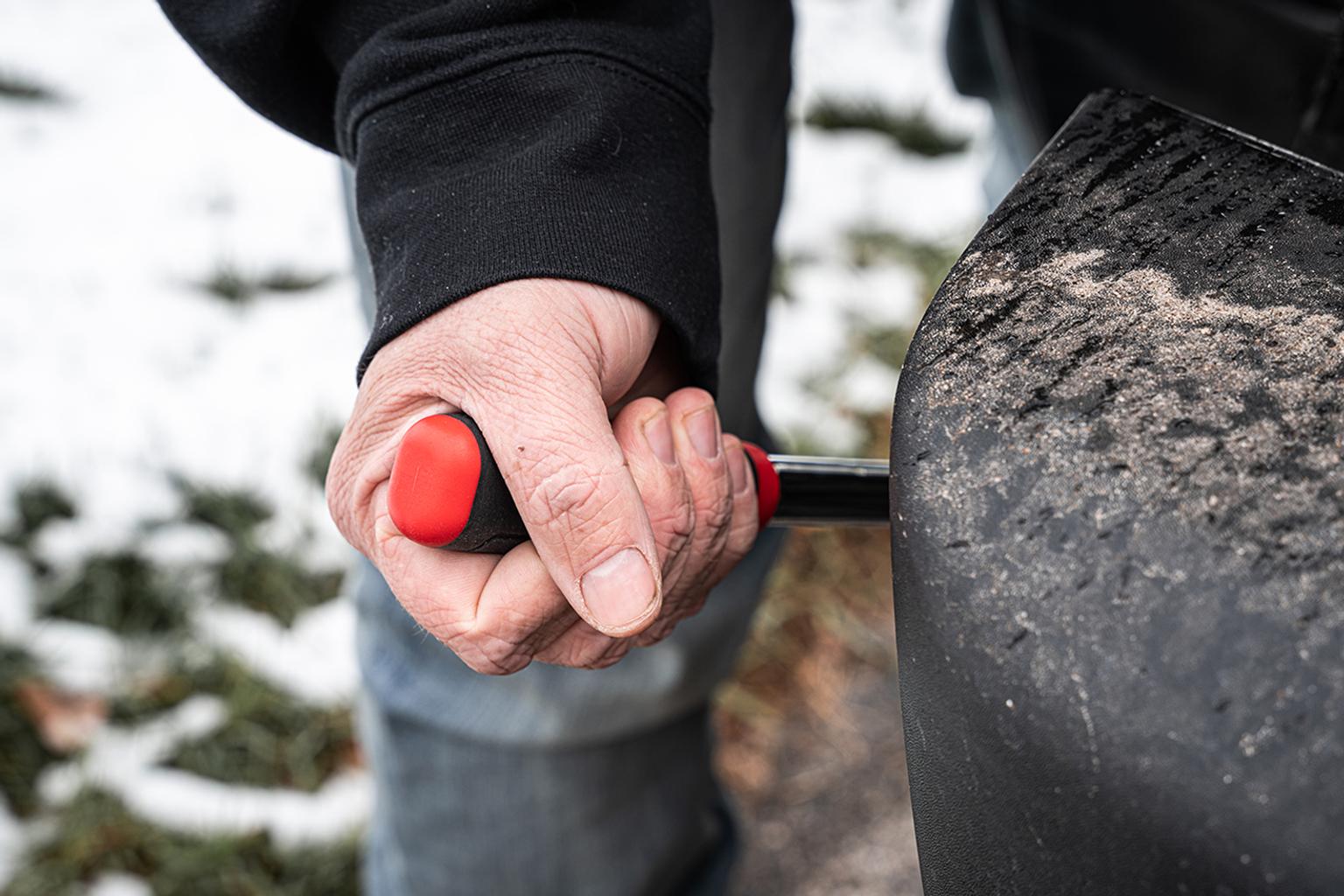 A man using a comfort grip breaker bar on a vehicle with snow in the background.